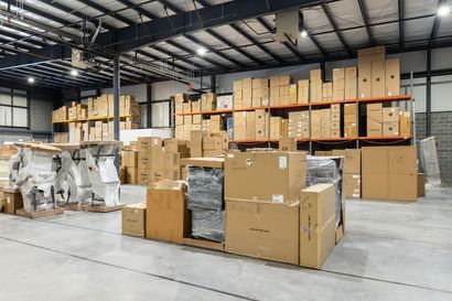 Warehouse interior with stacked cardboard boxes on shelves and the floor, under bright lights. Warehouse interior with stacked cardboard boxes on shelves and the floor, under bright lights.