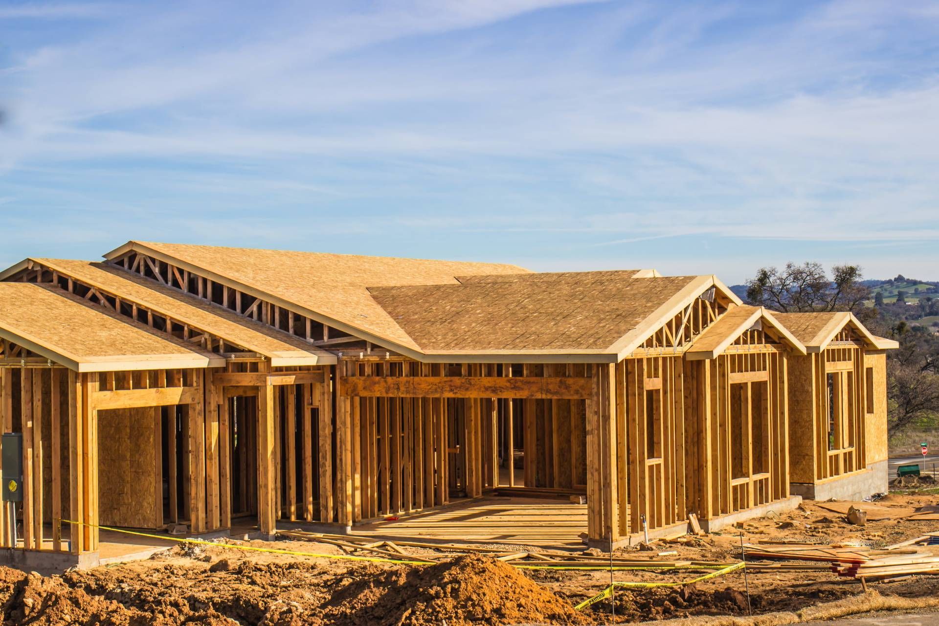 Wooden framework of a house under construction on a dirt lot, against a blue sky.