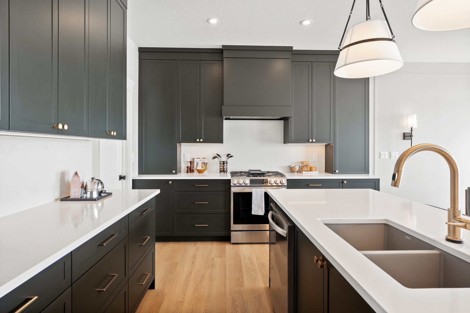 Dark gray kitchen cabinets with white countertops, stainless steel appliances, and gold fixtures.