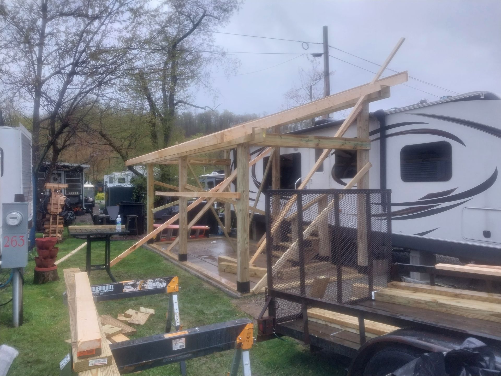 Construction of a wooden carport next to an RV on a trailer, outdoors.