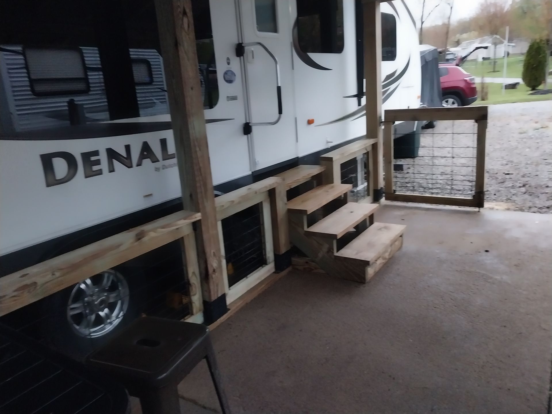 RV with wooden stairs and porch-like structure. A small gate is open next to the steps.