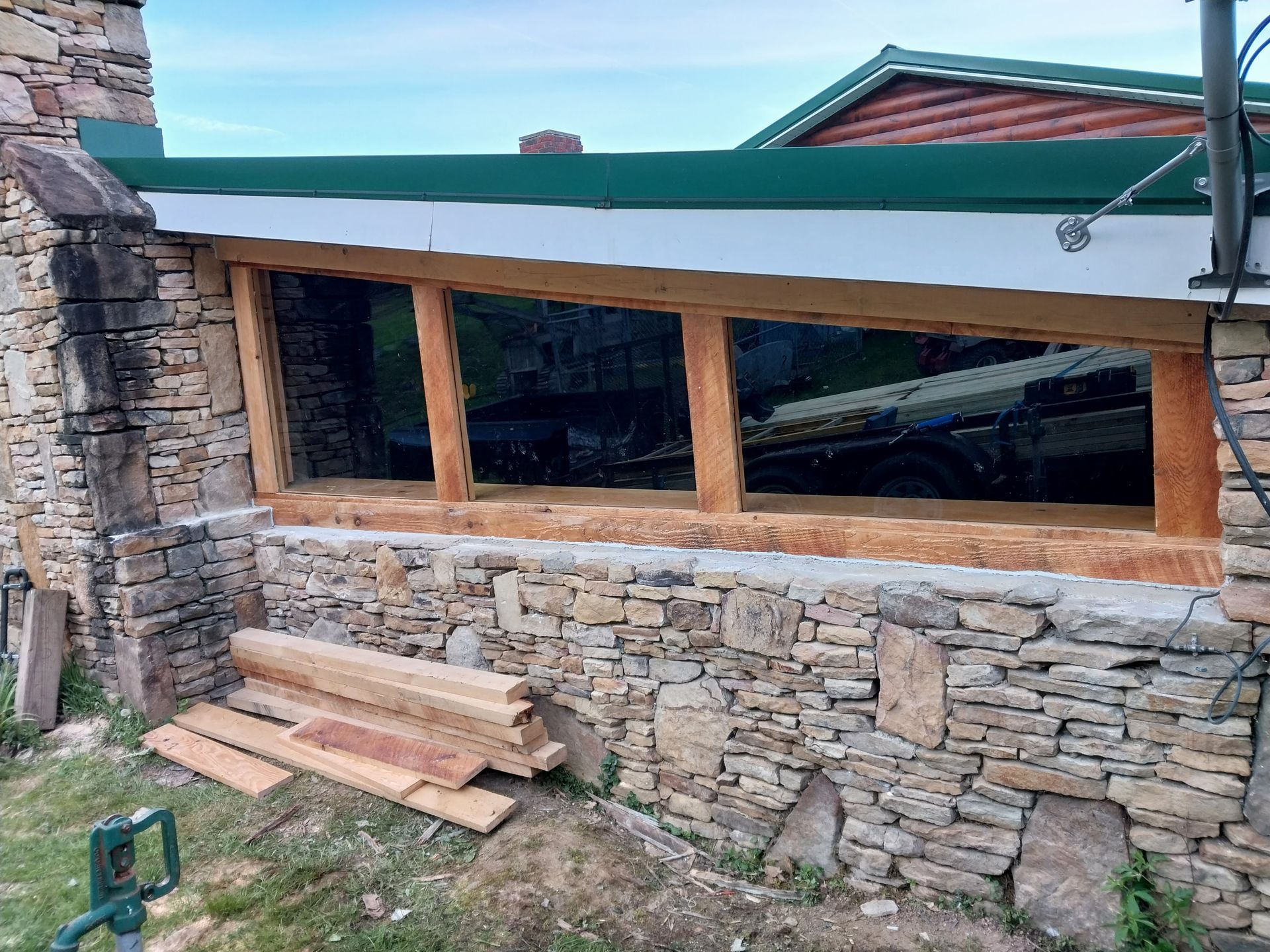 Stone wall with large rectangular window frame under construction; wood planks lie nearby.