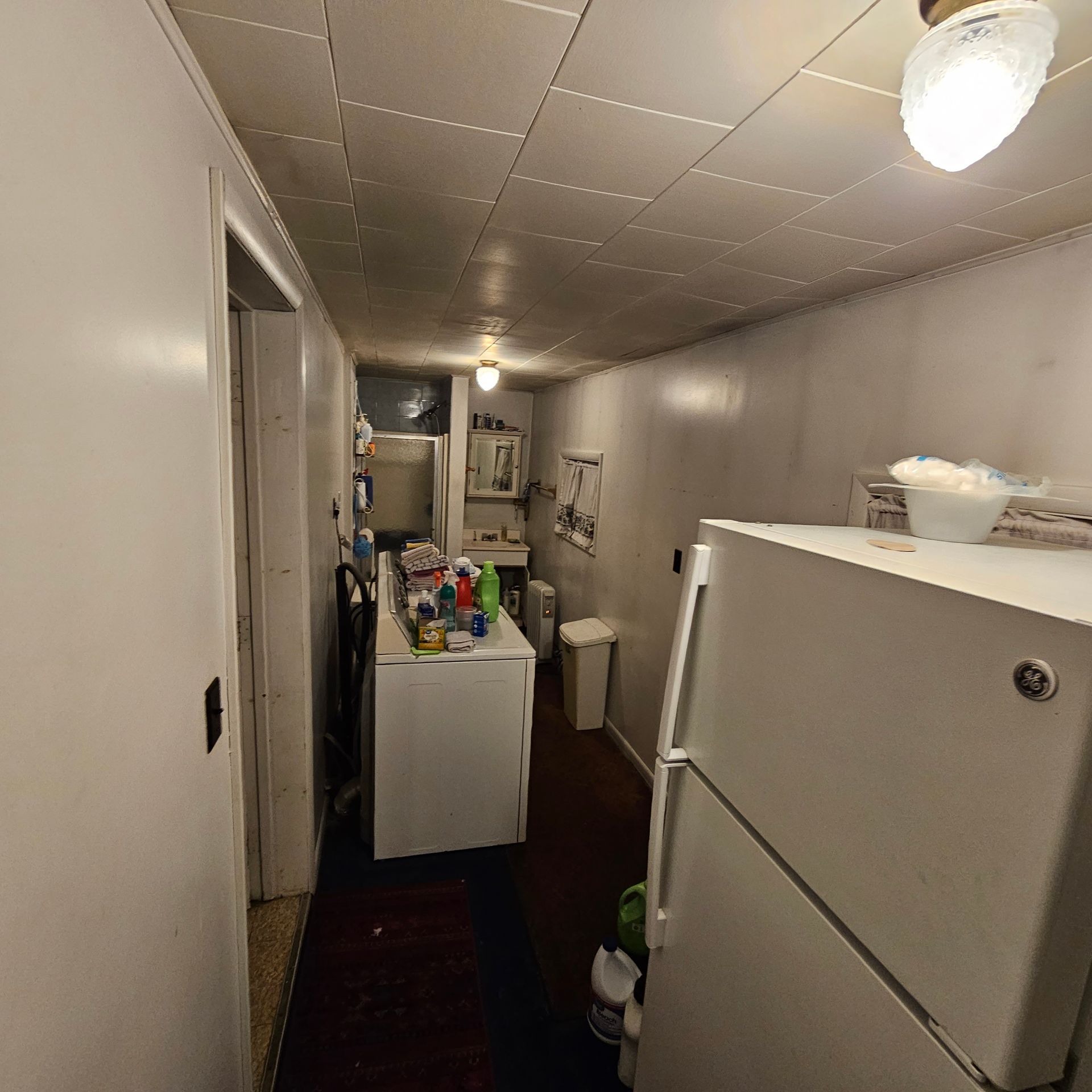 Narrow, cluttered kitchen with refrigerator, cabinets, and open doorway.