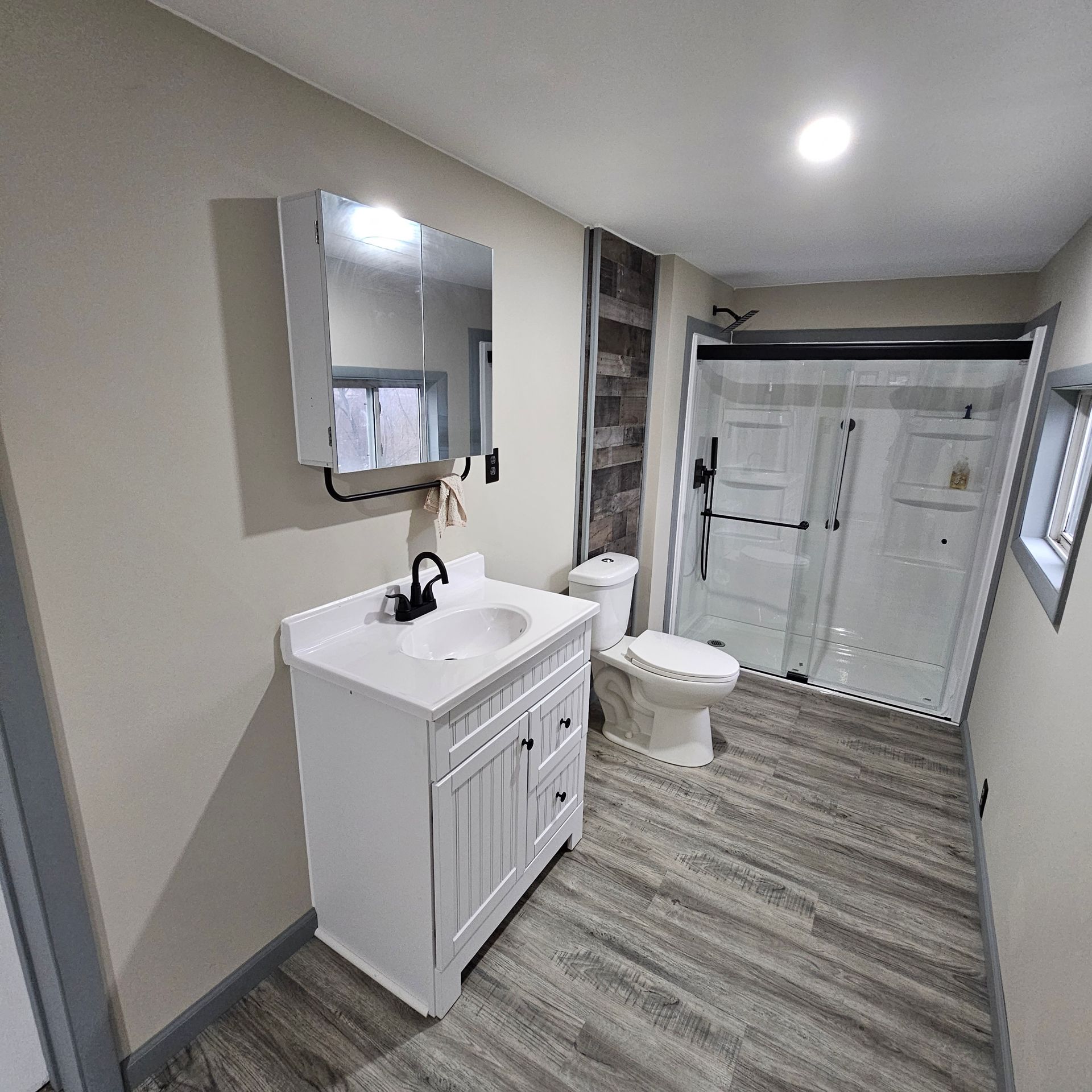 Bathroom with white vanity, toilet, and shower. Gray wood-look floor, light walls.