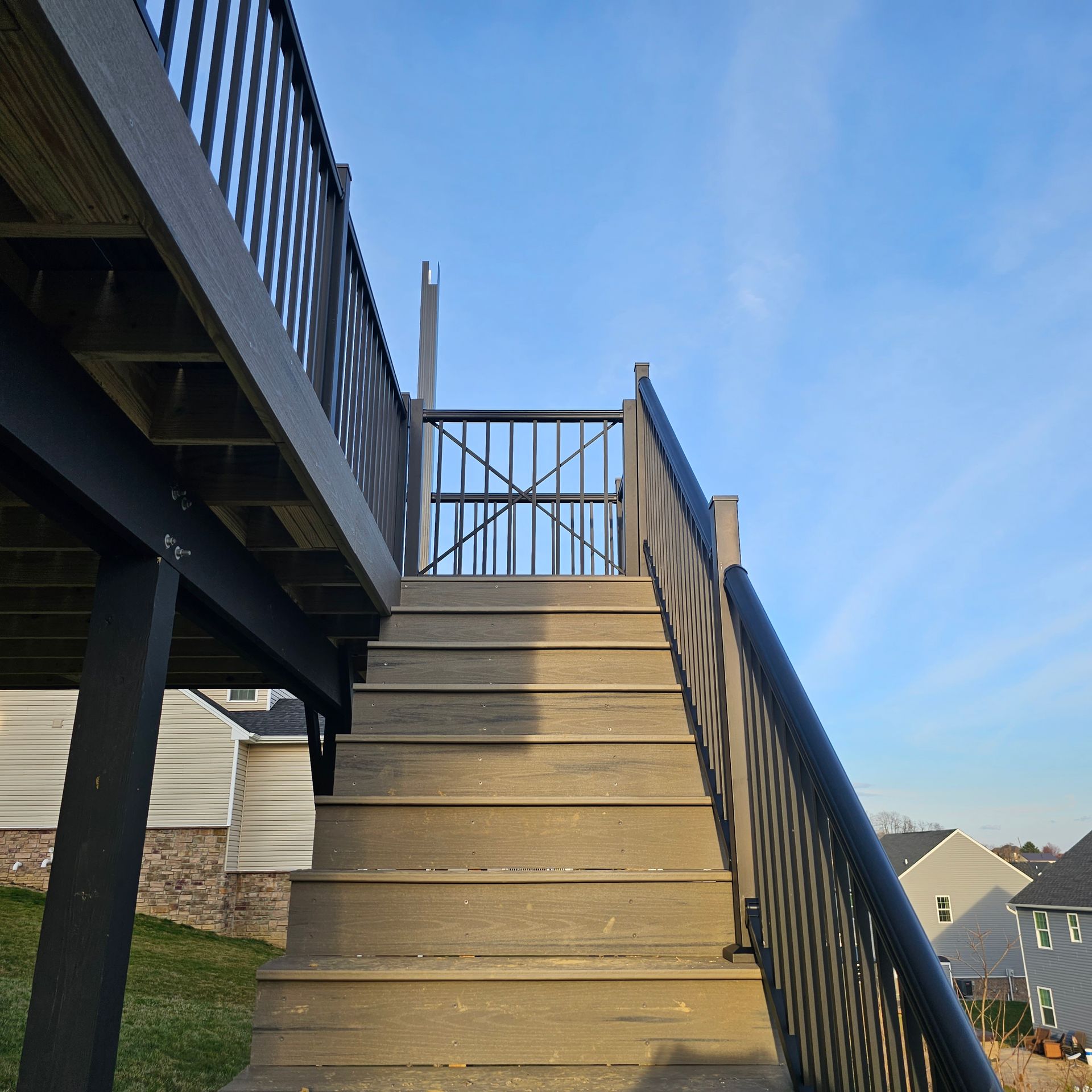 Wooden stairs with black railings lead up to a deck with a gate; blue sky.