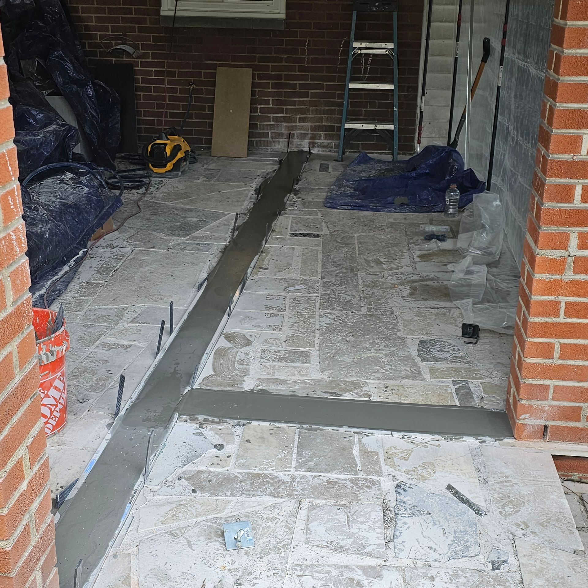 Brick patio under construction, with a long cement strip. Ladder and tools visible.