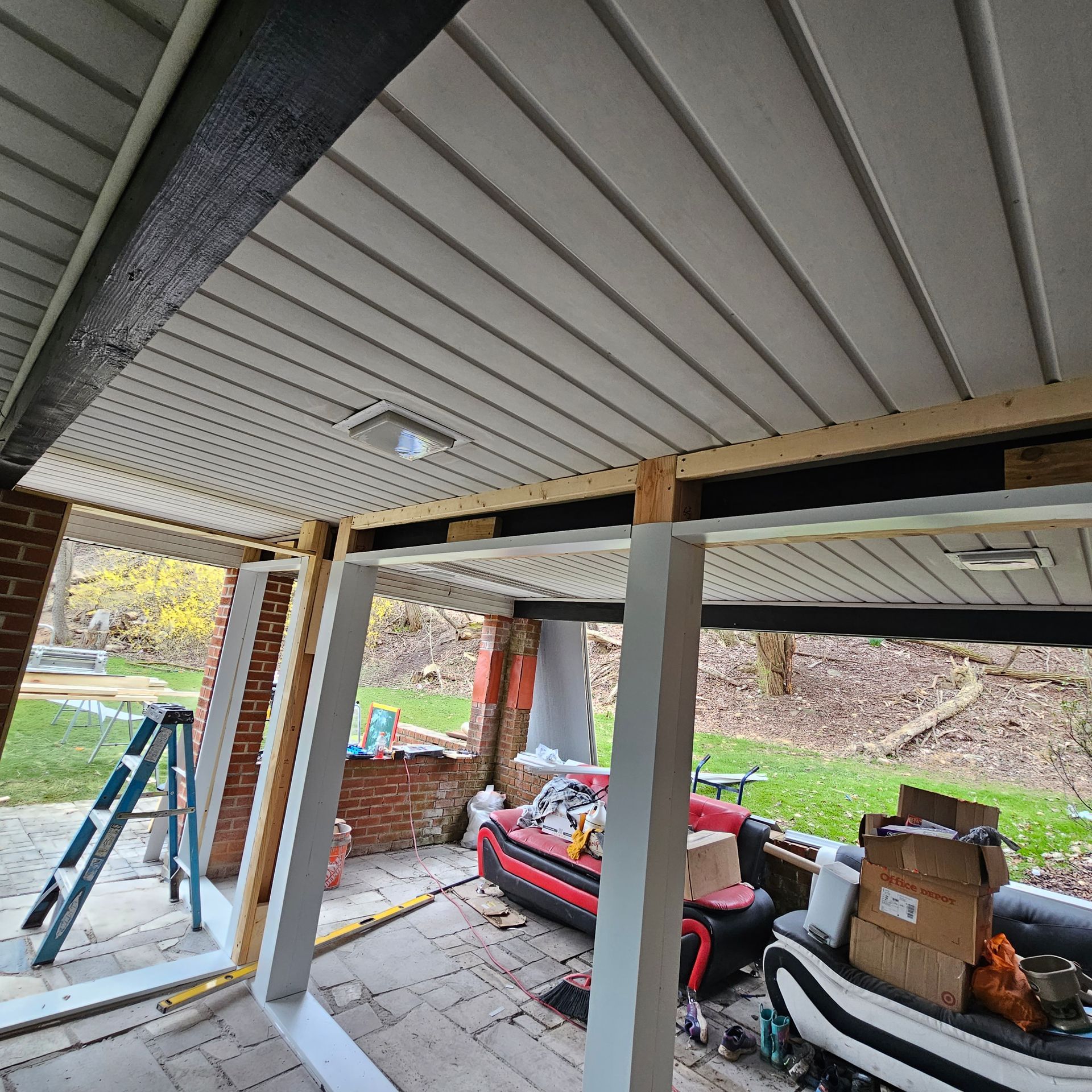 Construction site: building a porch. White framing, ceiling, and columns. Red brick wall.