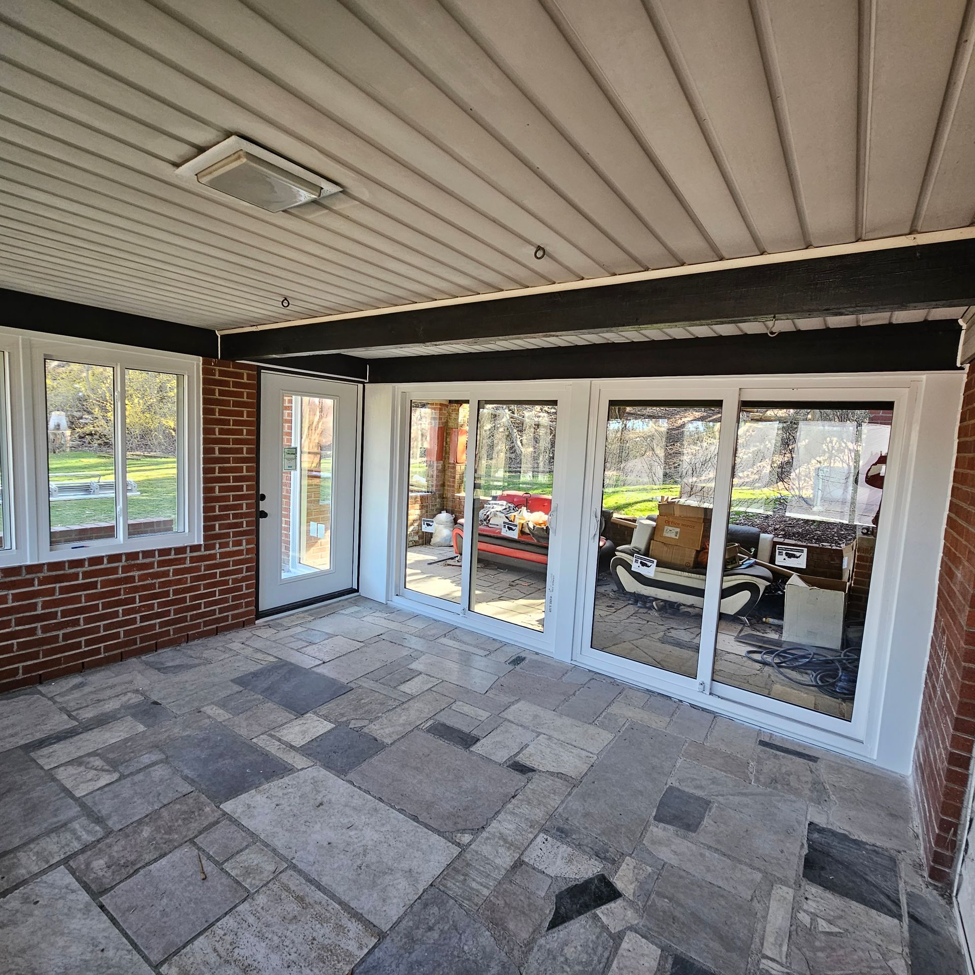 Sunroom with stone tile floor, white-framed glass doors and windows, brick walls, and a light-colored ceiling.