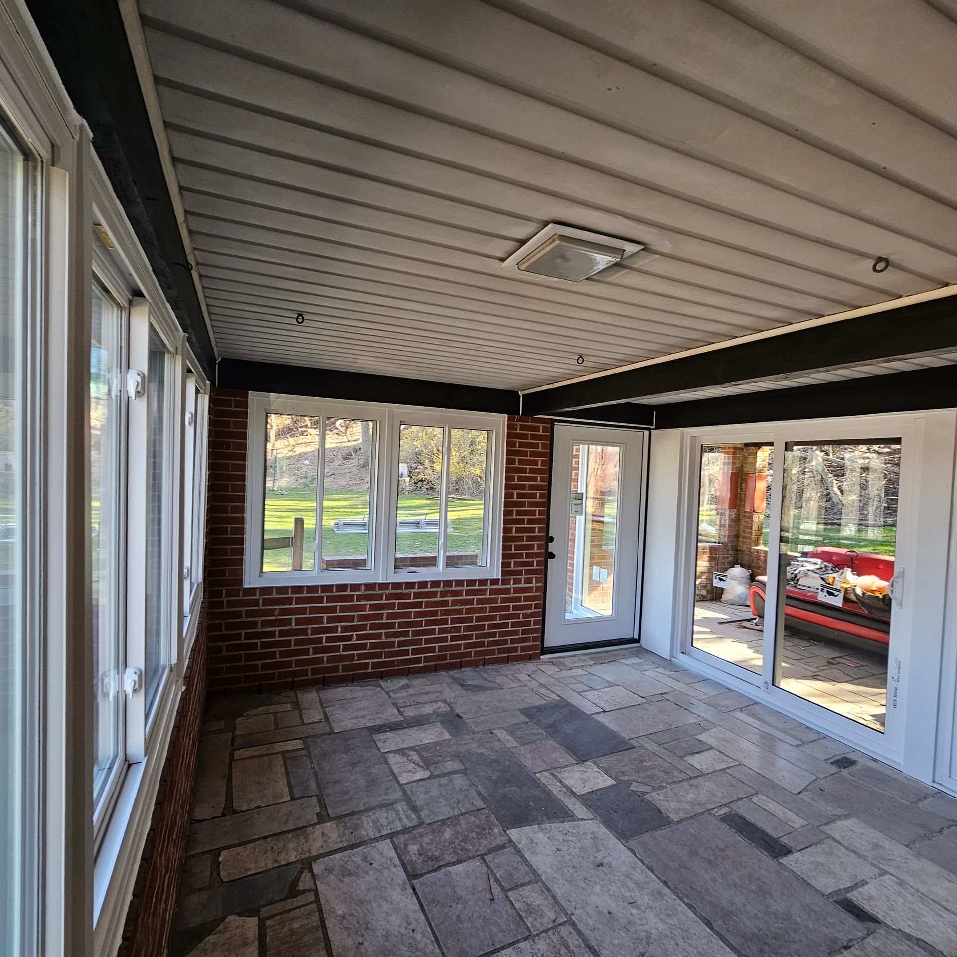 Sunroom with stone floor, brick wall, and large windows looking outside.