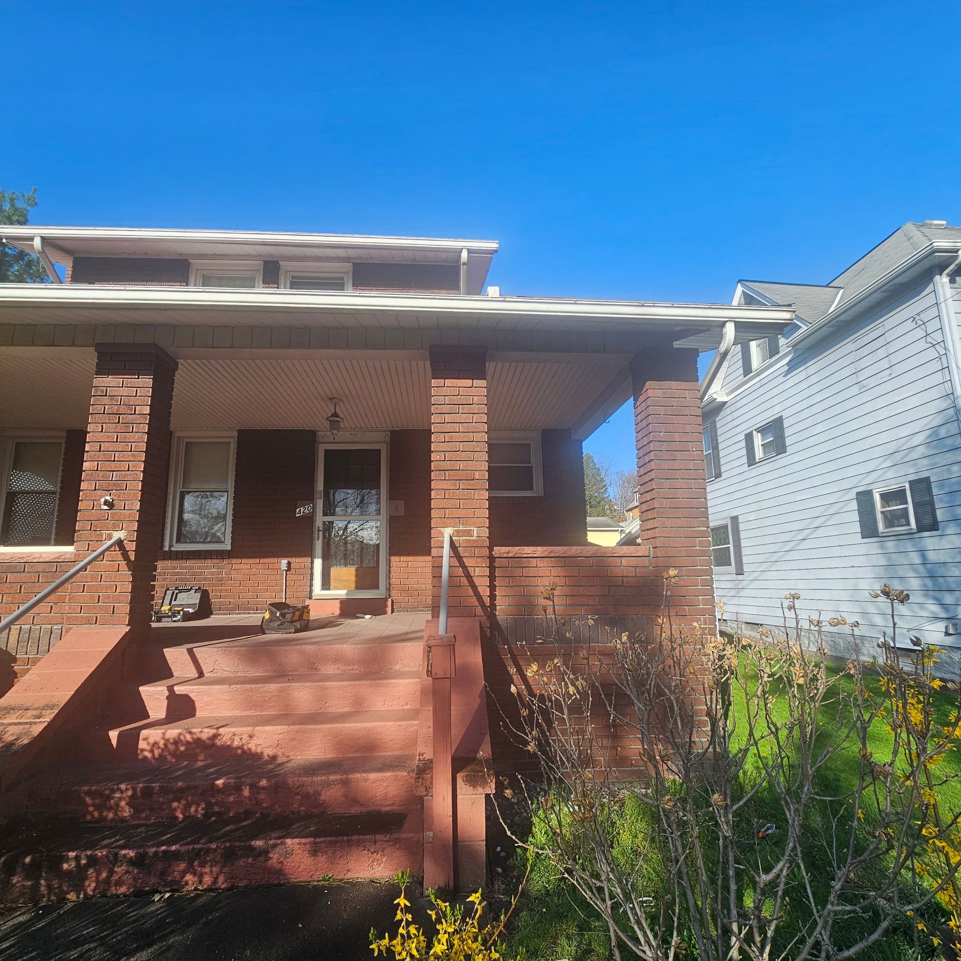 Brick house with porch and steps, door with window, blue sky.