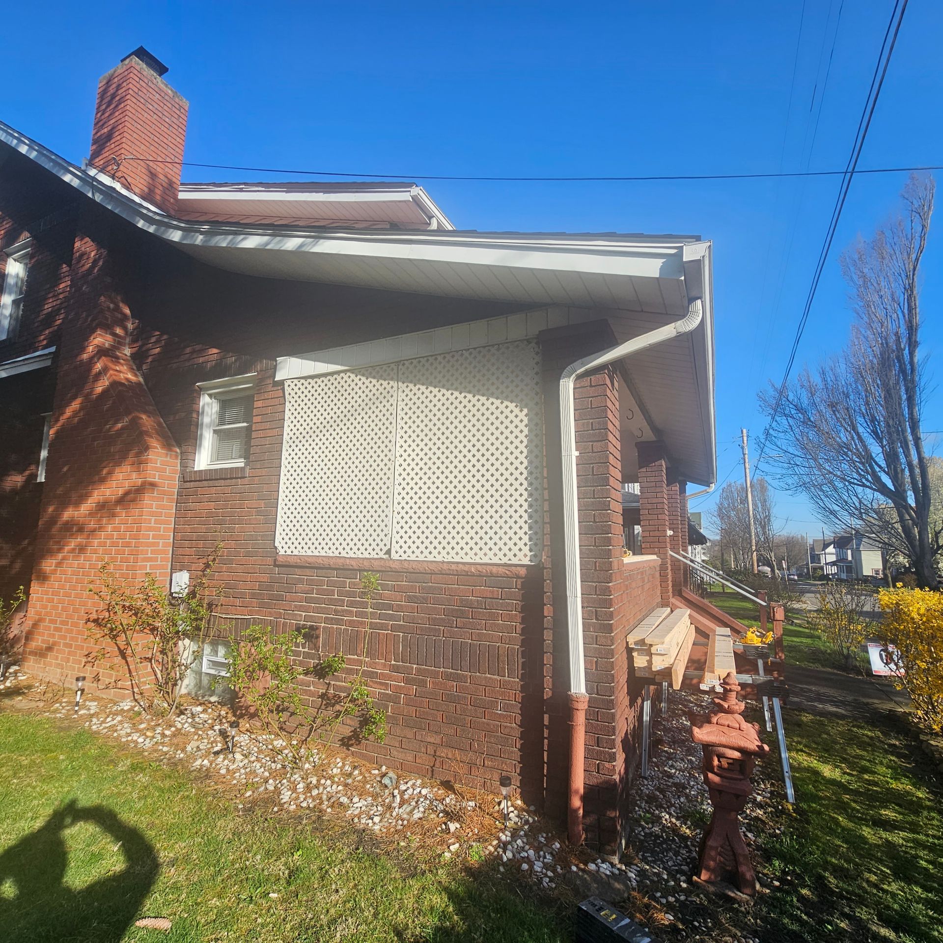 Brick house with white latticework over a window and a red brick chimney, set on a grassy lawn under a blue sky.