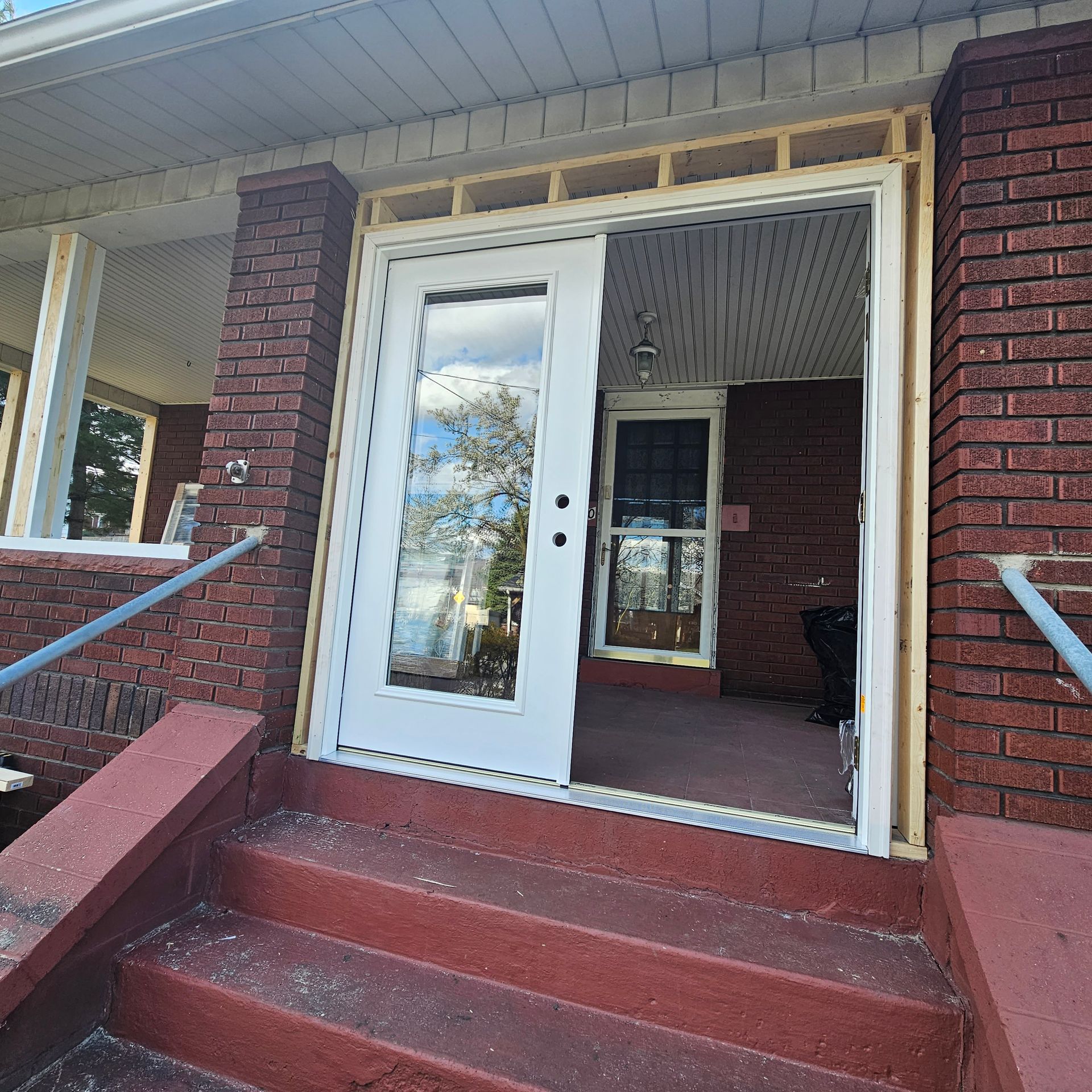 Exterior view of house with a doorway. A partially constructed door frame and white door are visible. Red brick, steps, and porch are also present.
