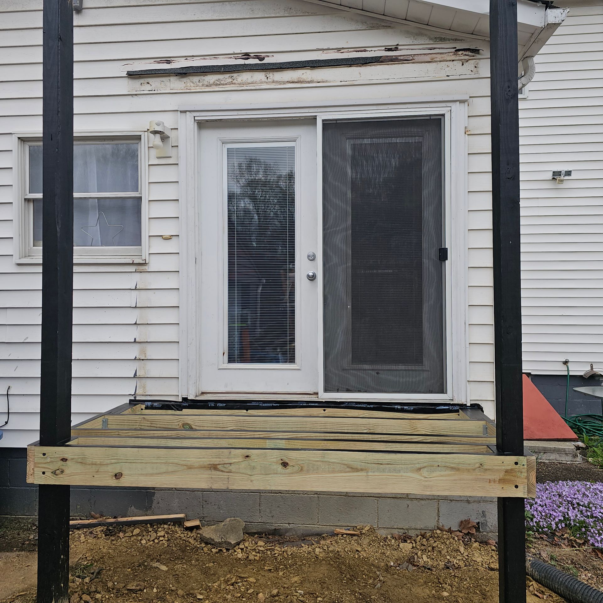 Wooden porch with a sliding door and a screen door, black support beams.