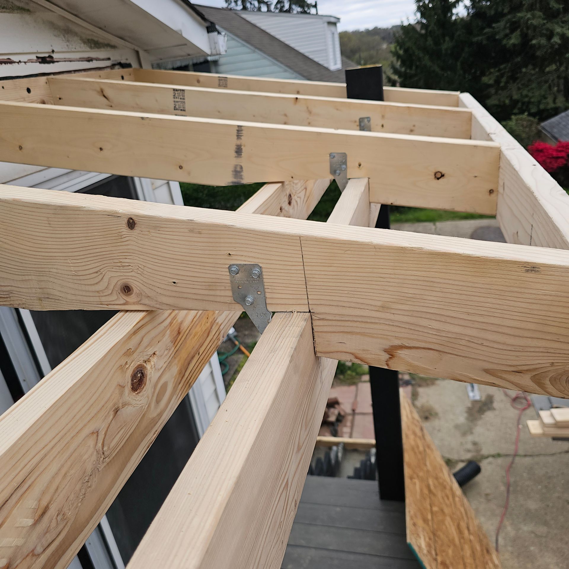 Wooden framework of a roof under construction, with beams and metal brackets.