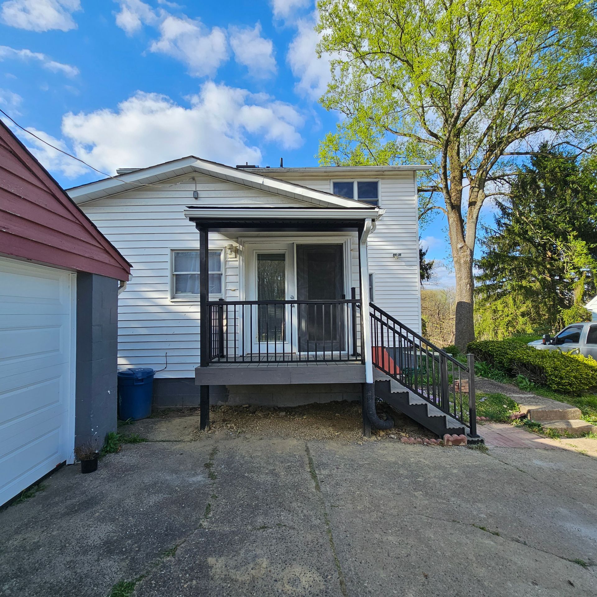 Back of a white house with a porch and black railing. A garage is on the left. Cloudy sky.