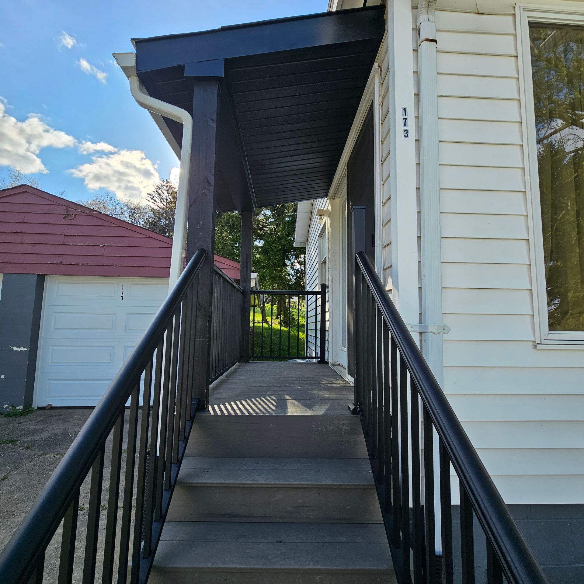 Exterior view of a white house with a covered entrance, black railing, and steps leading up.