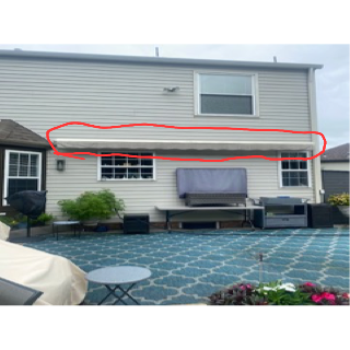 Back of a two-story beige house with a red-outlined awning above two windows. A backyard patio with furniture is in the foreground.