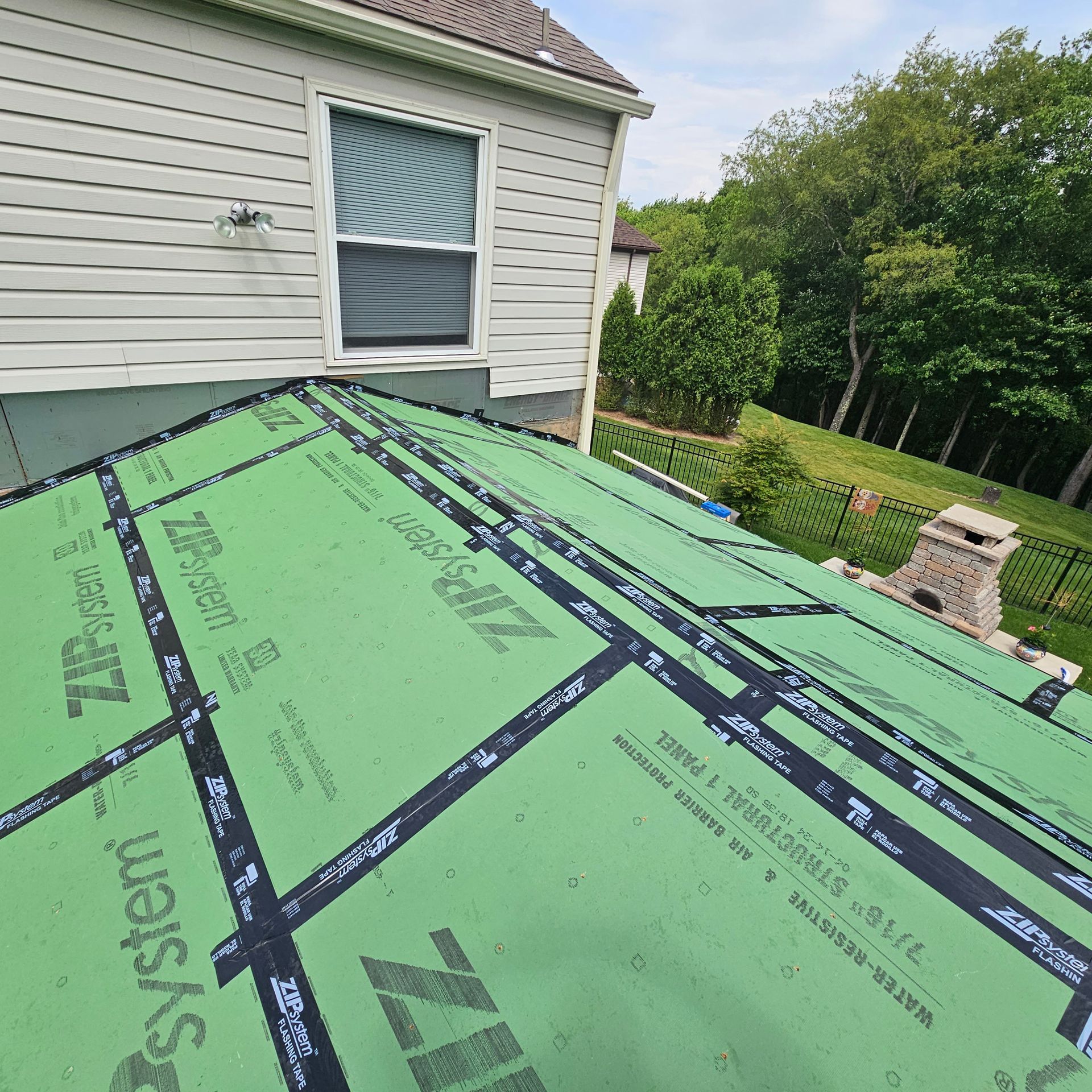 Green roofing material being installed on a house roof near a window and trees.