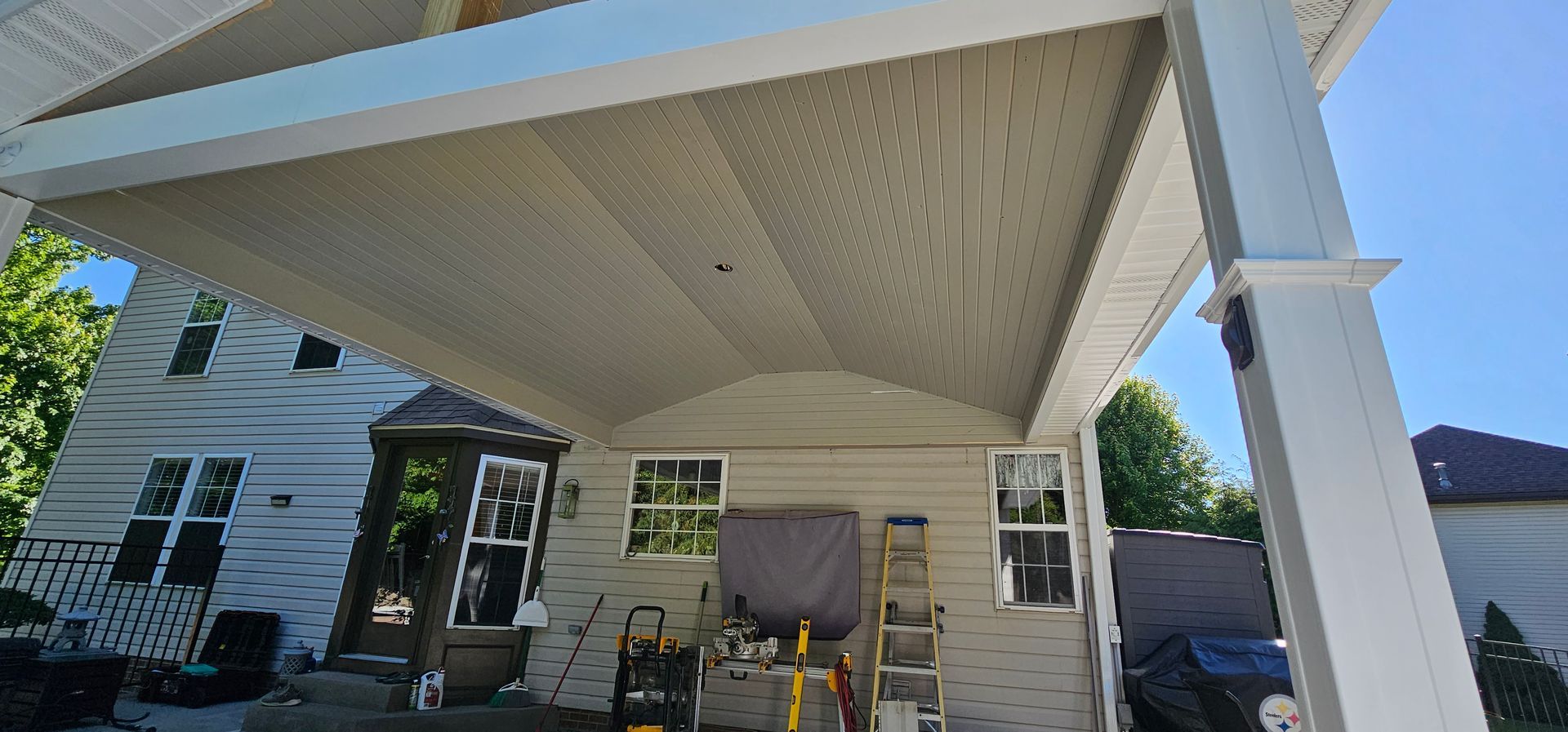 A covered patio with white columns adjoins a beige house. Blue sky overhead.