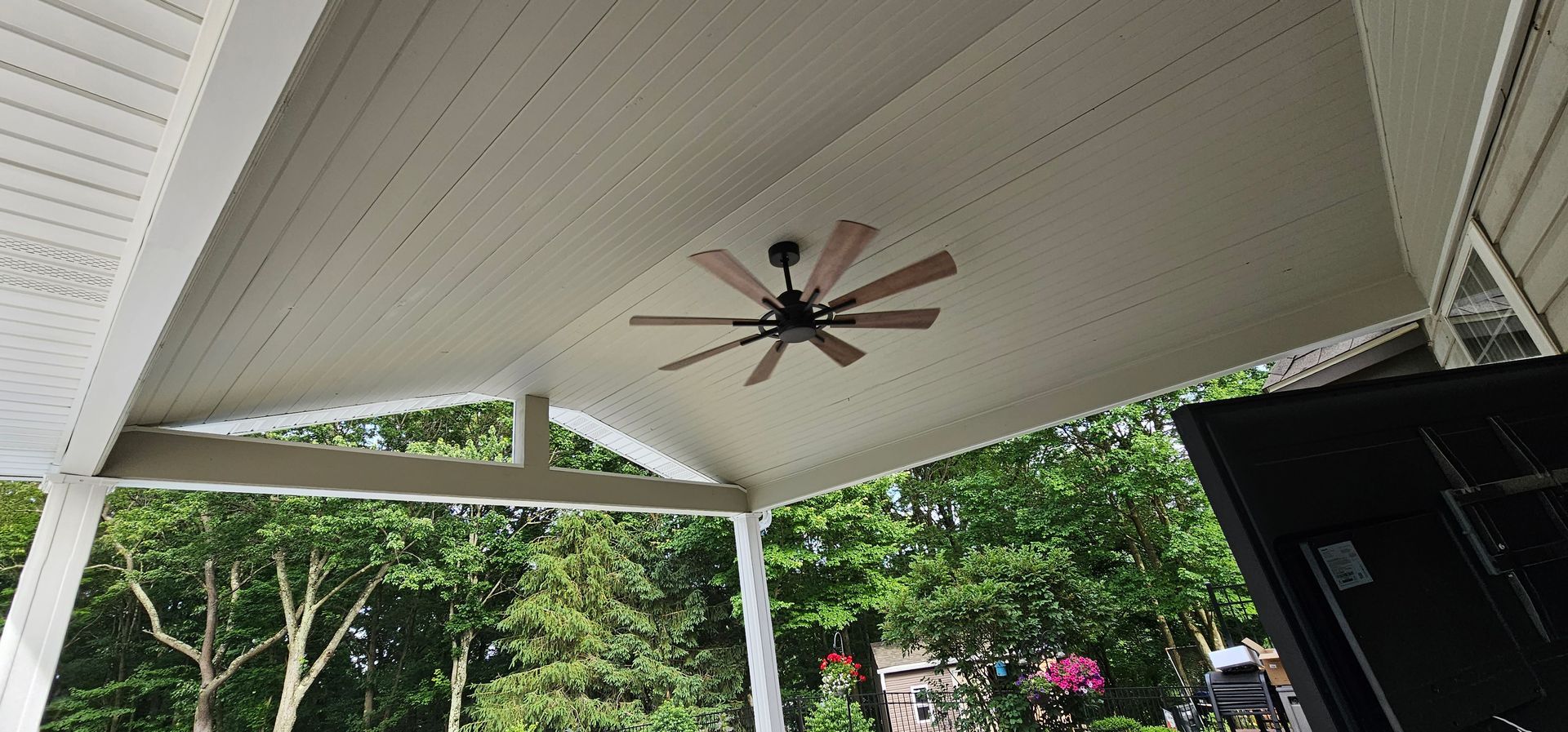 Porch ceiling with a ceiling fan. Trees are in the background.
