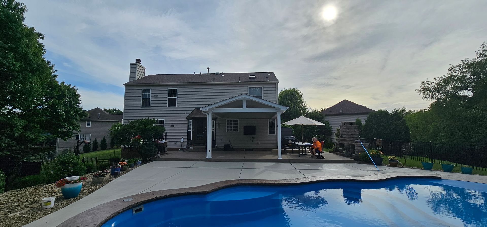 Backyard with pool, patio, and house under a cloudy sky.
