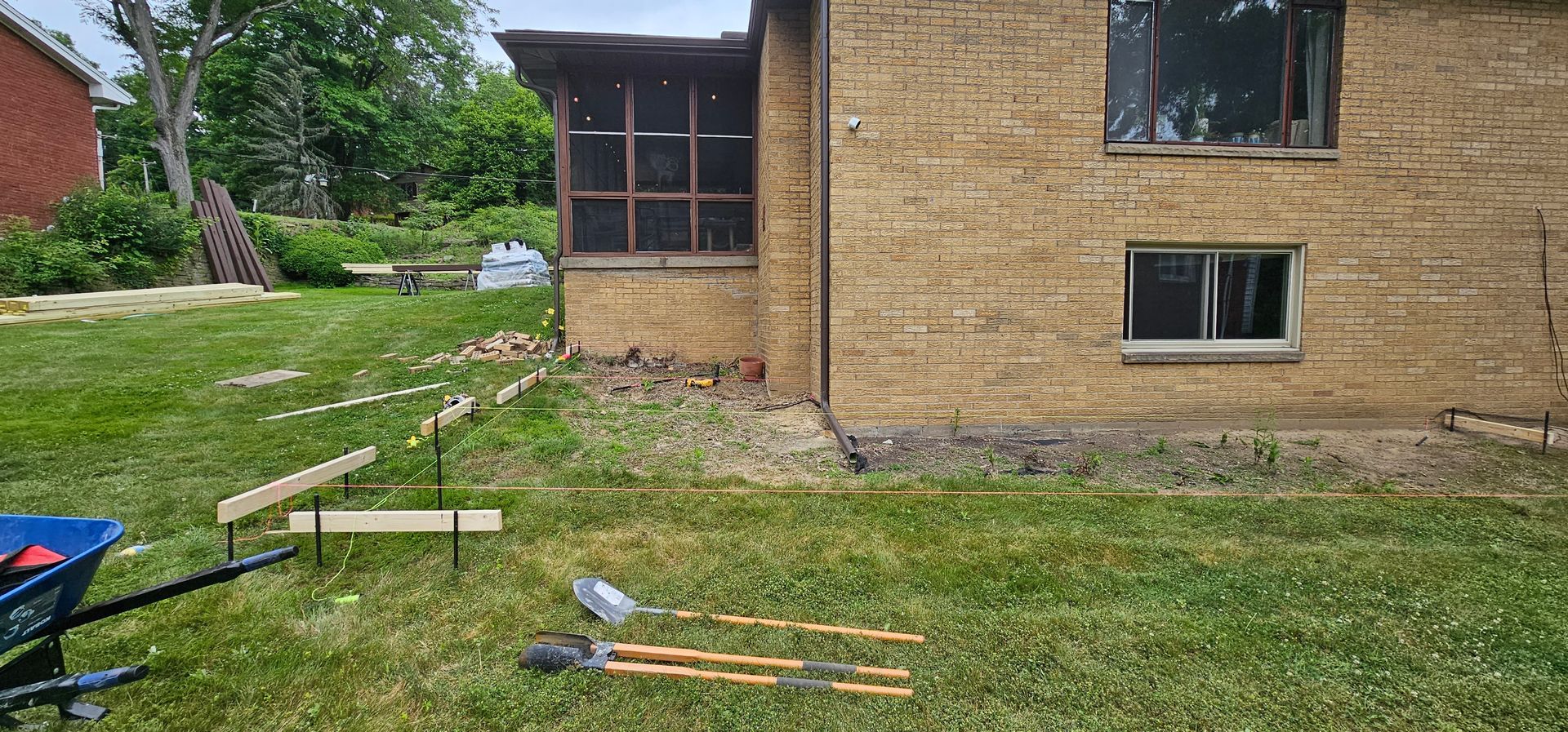 A building with layered tan walls and two windows, with tools laid out on the green grass.