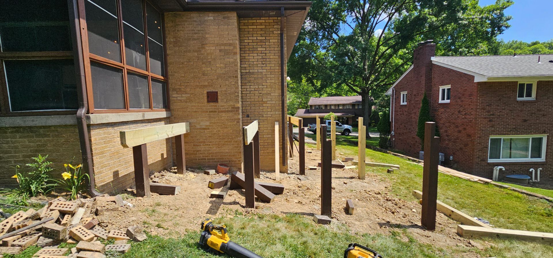 Construction site with wooden posts set in the ground, next to a brick building and grass lawn.