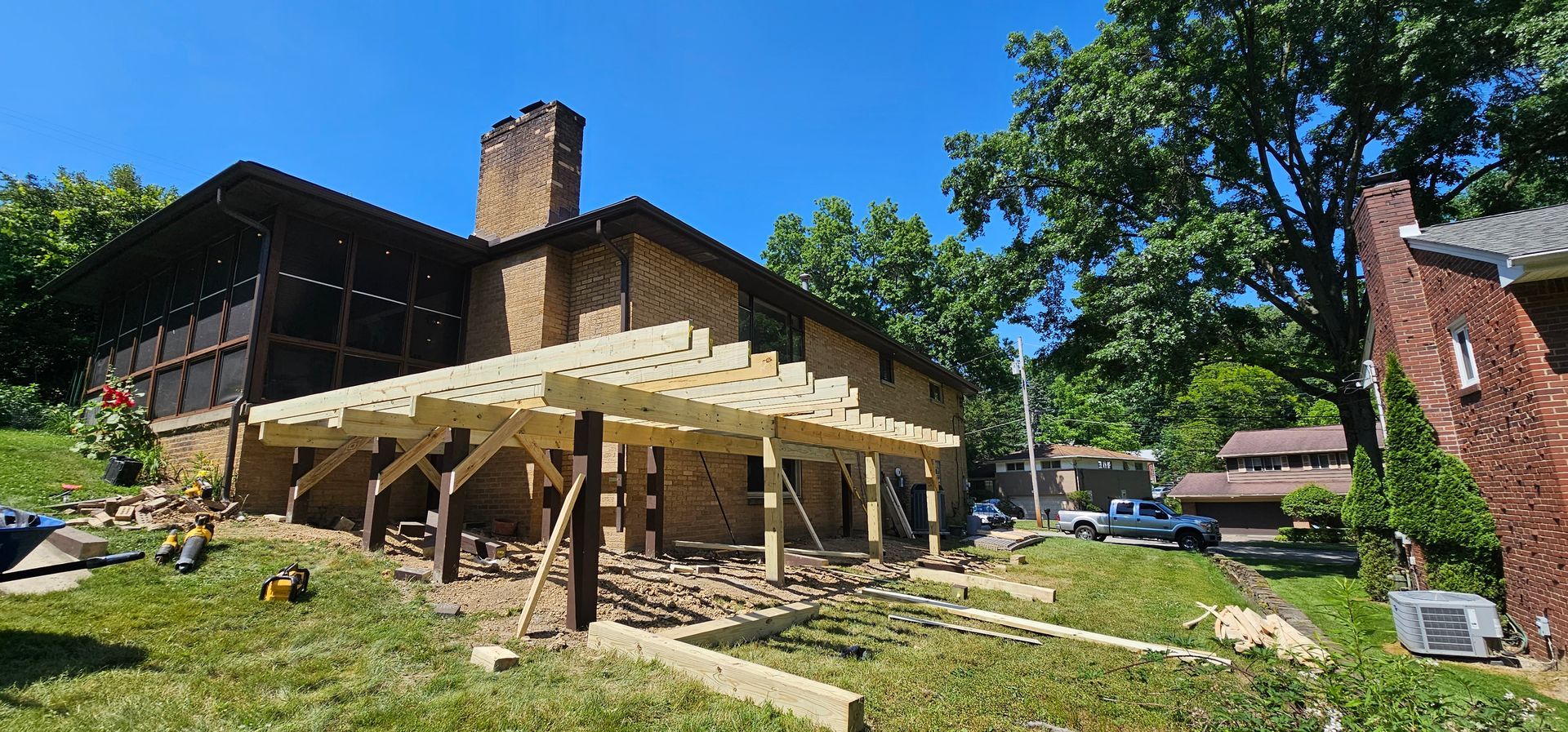 Construction of a deck on a two-story brick house with a chimney. Blue sky and green trees in the background.