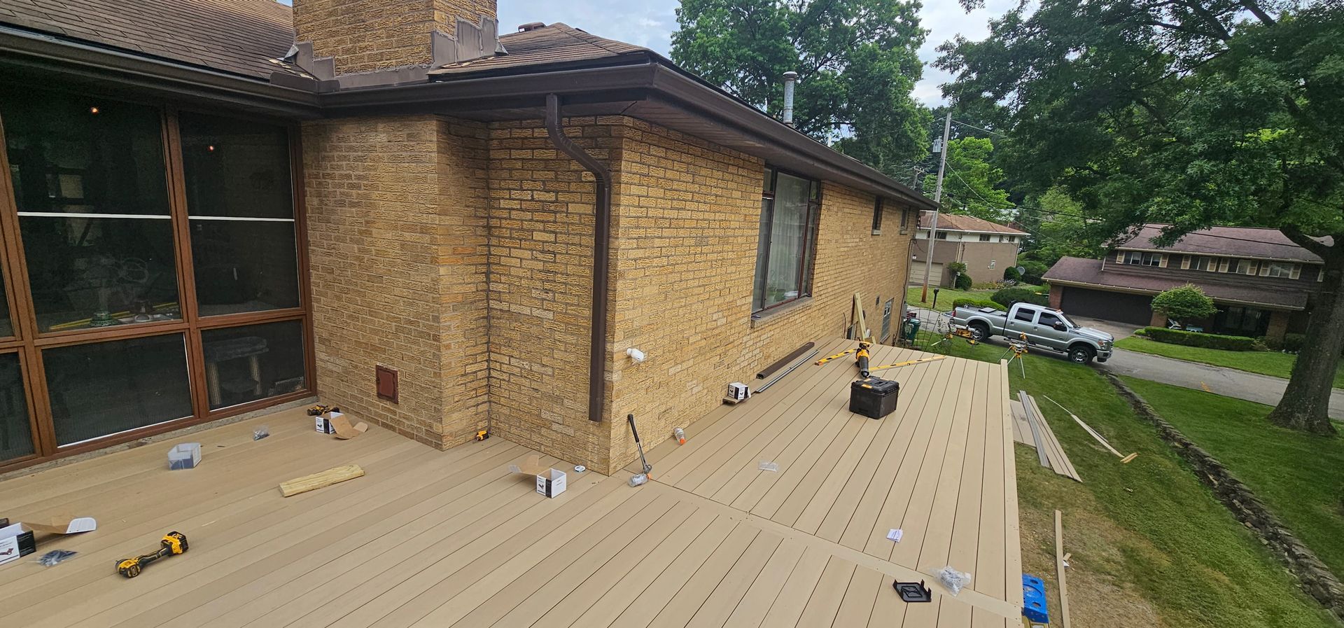 Deck construction underway next to a brick house, with a truck visible in the distance.