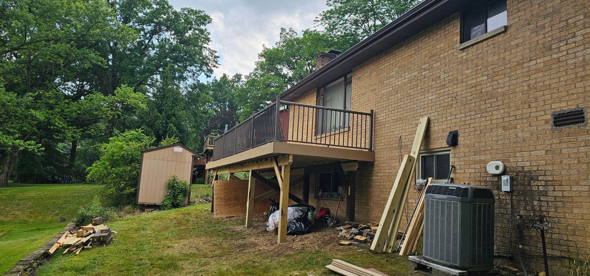 A deck attached to a brick house is under construction with lumber on the ground.