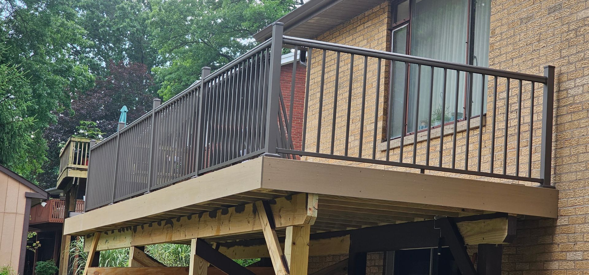 Brown deck with railing in front of a brick building.