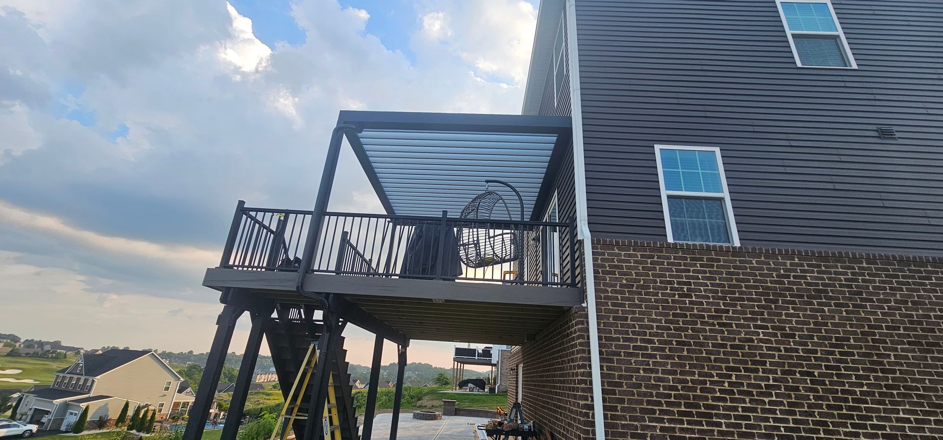 A two-story house with a deck and a shaded pergola. The house is brick and gray siding. Cloudy sky.