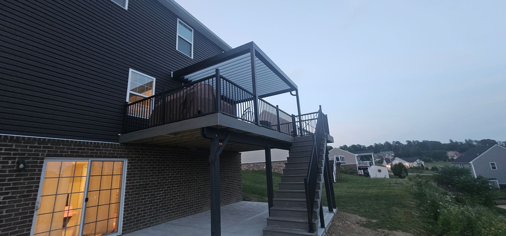 A house with a deck and stairs. The house is brick. The deck has a pergola.