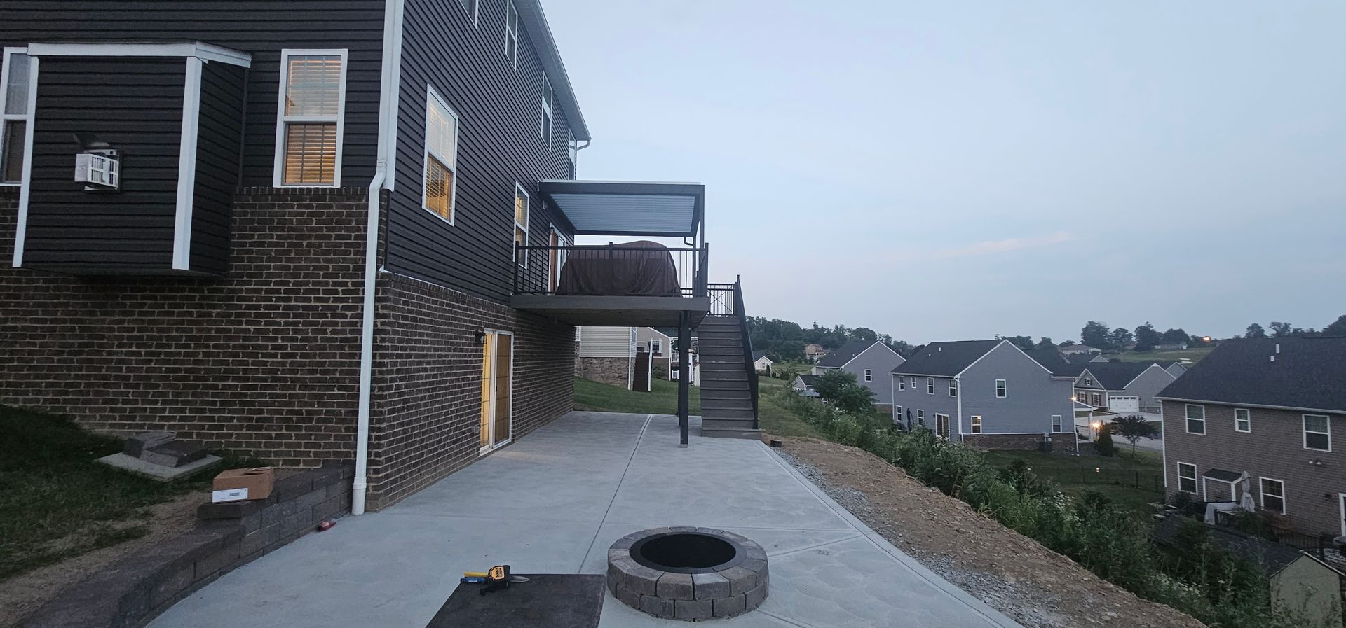 Exterior of a house with a deck, concrete patio, fire pit, and view of neighboring houses.