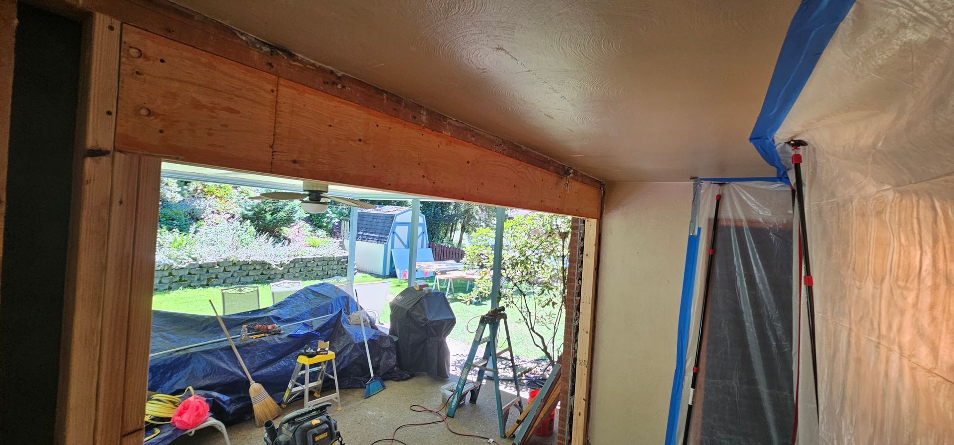 Interior view of a room under construction with exposed wooden beams, open window, and protective plastic sheeting.