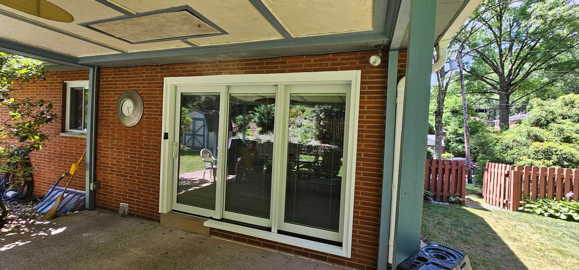Patio with brick wall, glass doors, and a small fence in a backyard.