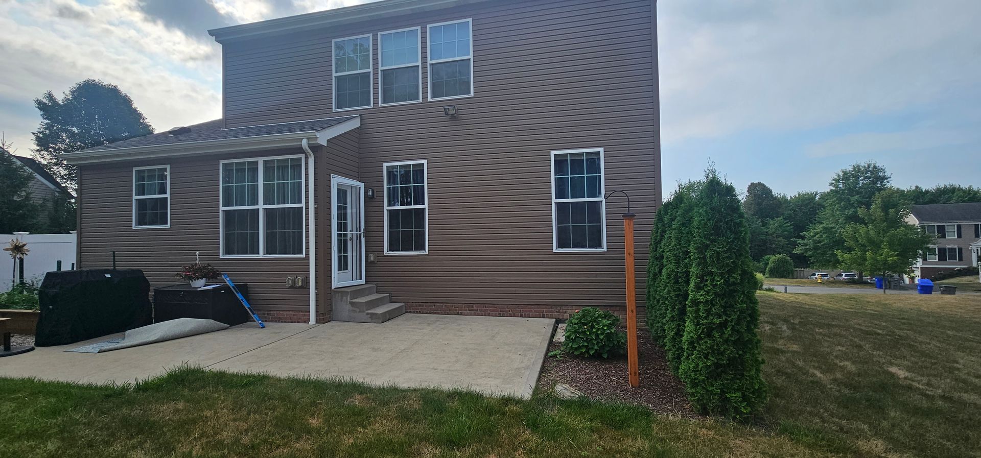 Back of a brown house with windows and a door, a concrete patio, and a grassy lawn.