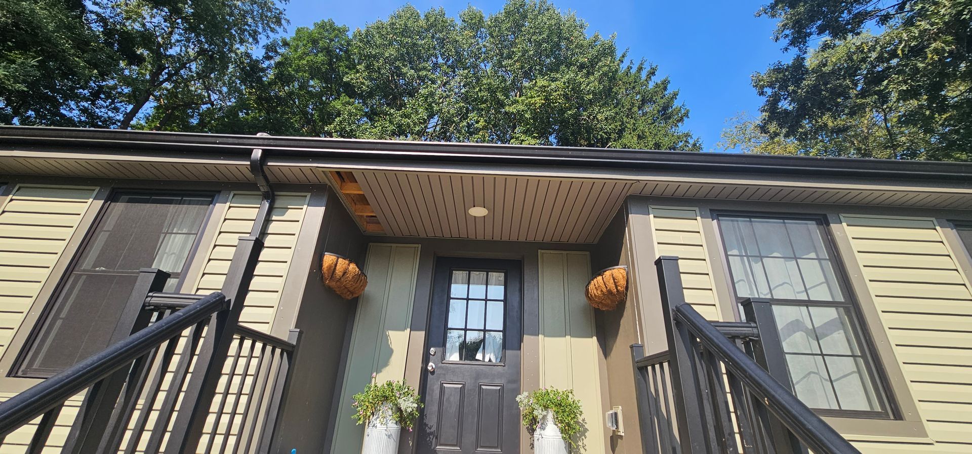 House entrance with black door, stairs and railings. Two hanging baskets with pumpkins. Green siding.
