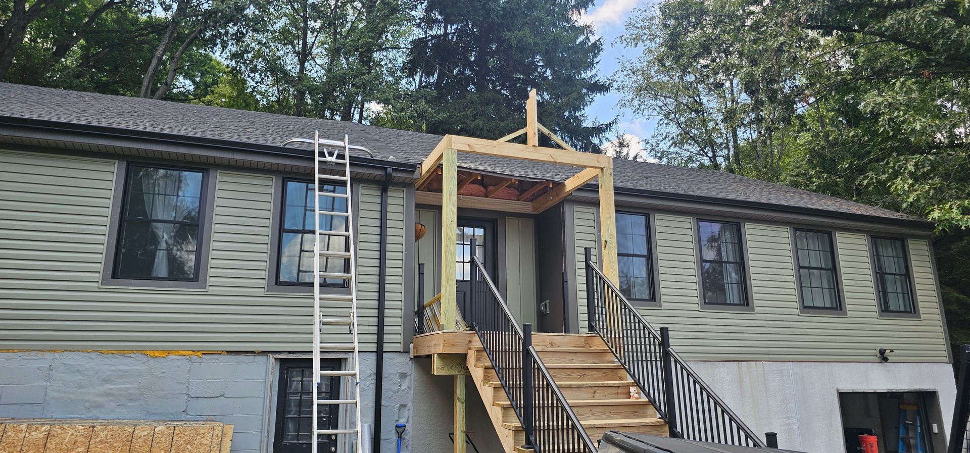 House with wooden porch under construction; ladder on the side.