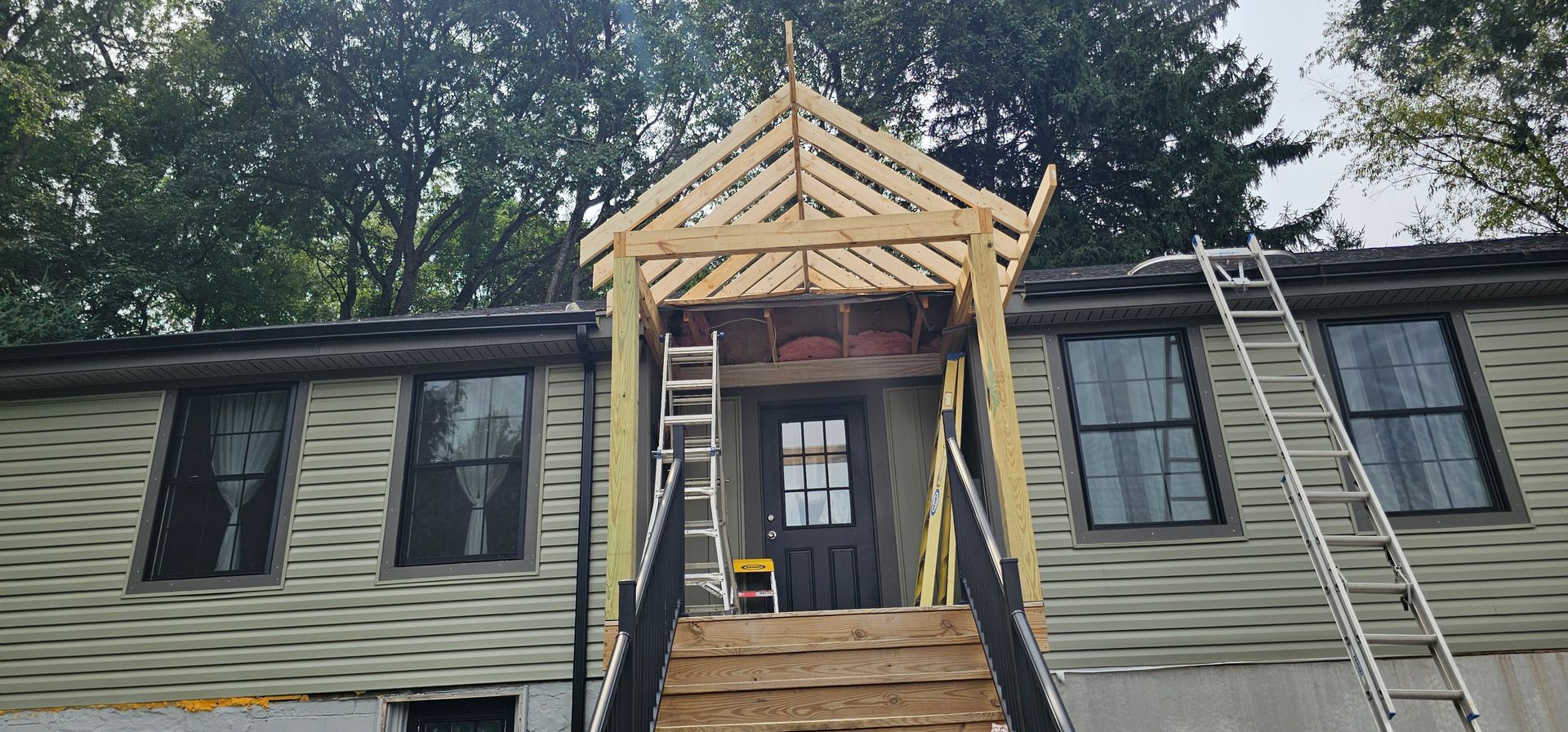 House under construction with a wooden porch roof over the front door and staircase.
