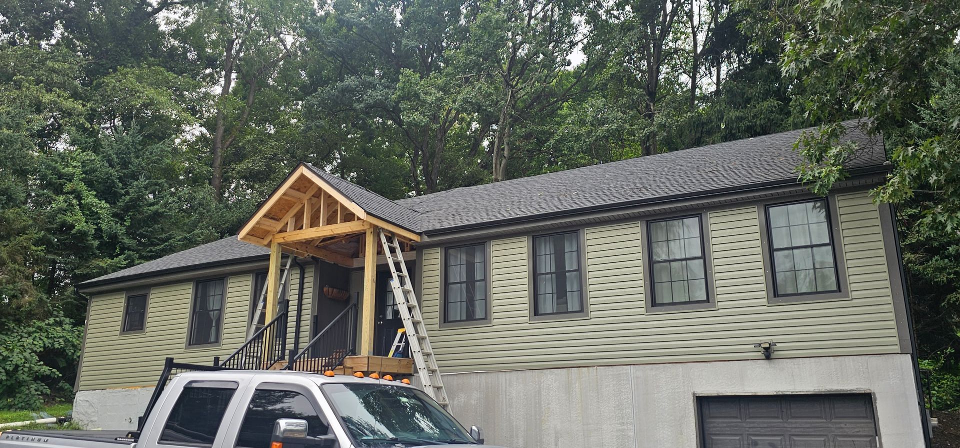 House under construction with a new porch and siding, with trees in the background, a truck in front.