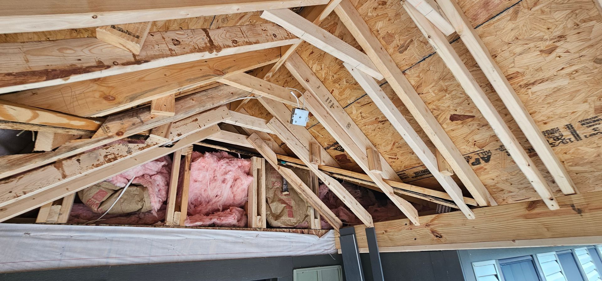 Framing of a roof in a building under construction. Brown wood, insulation, and angled supports are visible.