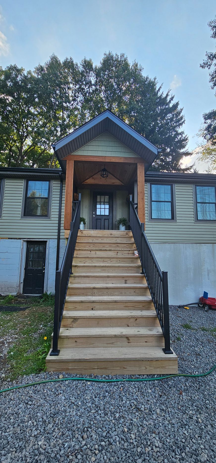 A house with stairs leading to the entrance, flanked by black railings and surrounded by trees.