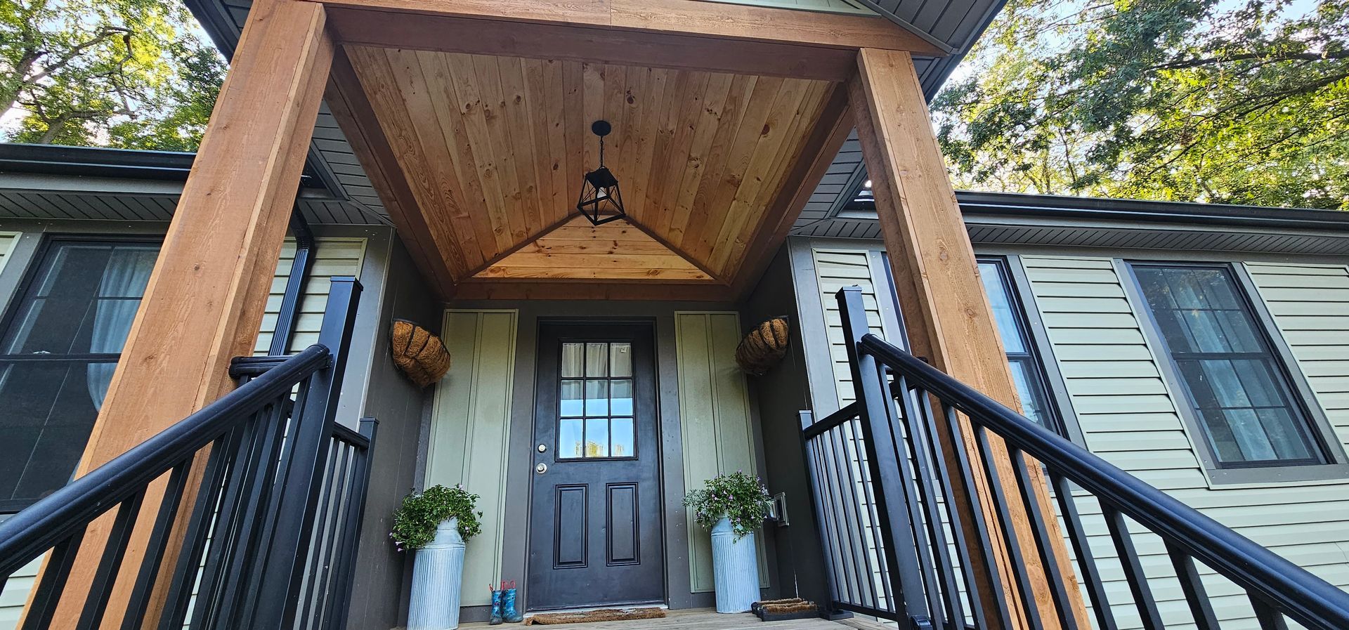 A house entrance with dark railing, brown wooden supports, and a hanging light fixture.