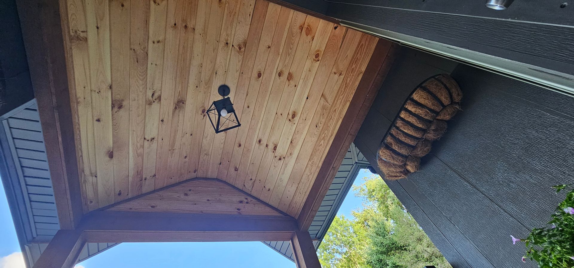 Wooden porch ceiling with a light fixture and a wasp nest on the wall.