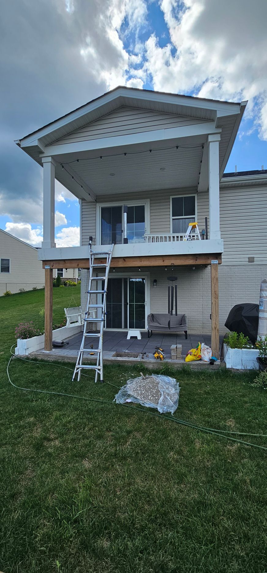 Back of a house with a deck and patio. A ladder leans against the deck. The sky is cloudy.
