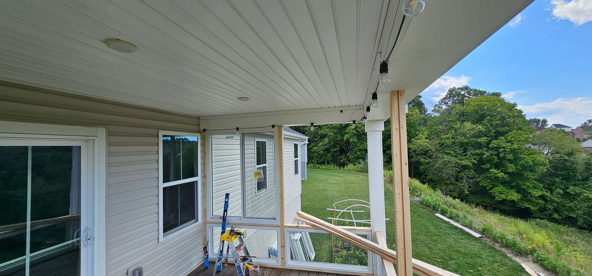 A covered porch with white siding, unfinished railings, and a view of trees and sky.