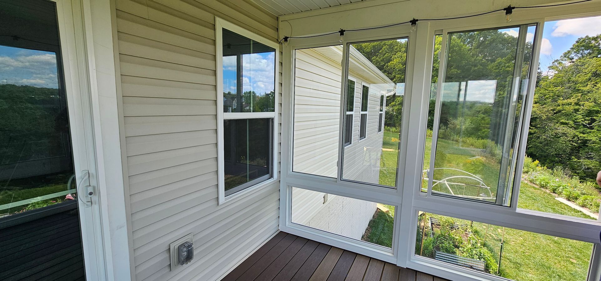 A screened porch with a window and view of a yard. Beige siding on the house.