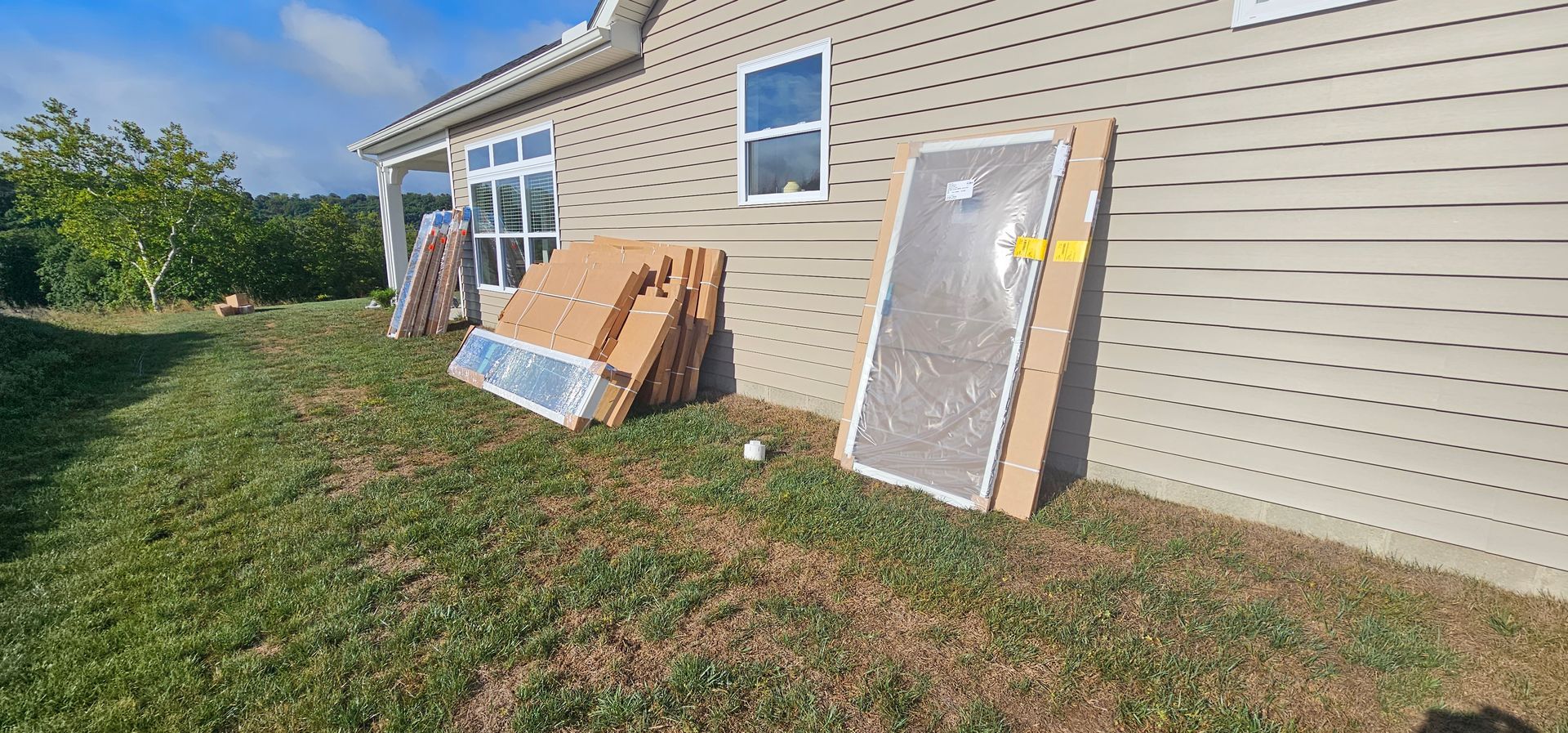 Several new doors leaning against the side of a house with light brown siding and a blue sky.