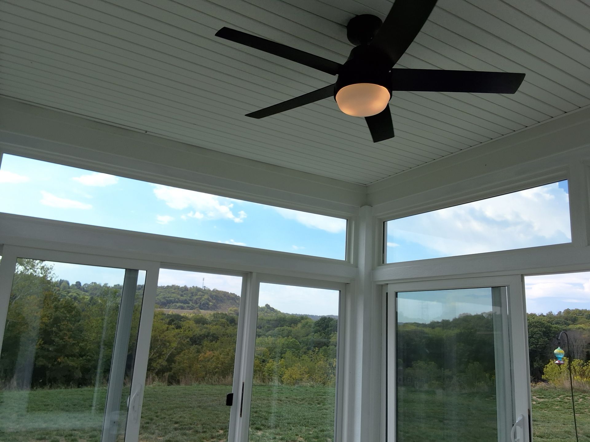 Sunroom interior with a ceiling fan, white trim, and a view of trees and sky.